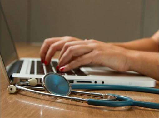 Image of healthcare worker at a desk on a laptop and virtual medical related icons floating on top
